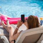 Vrouw zit met smartphone aan het zwembad.