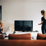 Twee vrouwen kijken in de living hoe ze tv kunnen kijken via een app.