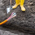 Persoon met gele laarzen staan aan een sleuf met een kabel in