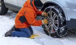 Man legt sneeuwkettingen op zijn autobanden.
