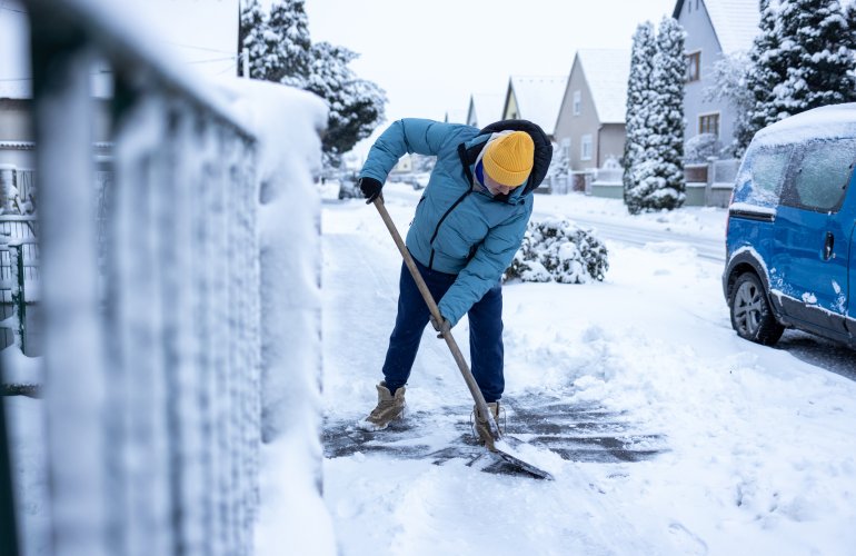 Actieve senior man maakt het voetpad sneeuwvrij met een sneeuwschop.