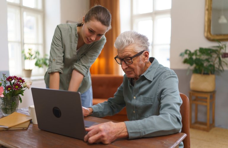 Oudere man sluit online een uitvaartverzekering af met behulp van zijn kleindochter.
