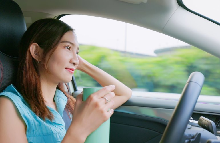 Vrouw zit achter het stuur in haar zelfrijdende auto terwijl ze koffie drinkt.