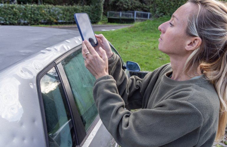 Vrouw trekt foto van hagelinslag op haar auto.